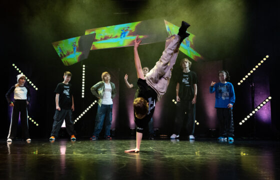 Chłopak tańczący breakdance na scenie, za nim grupa dzieciaków