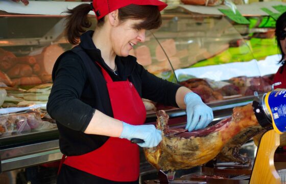 Młoda kobieta przed ladą z wędlinami i mięsem kroi plastry mięsa