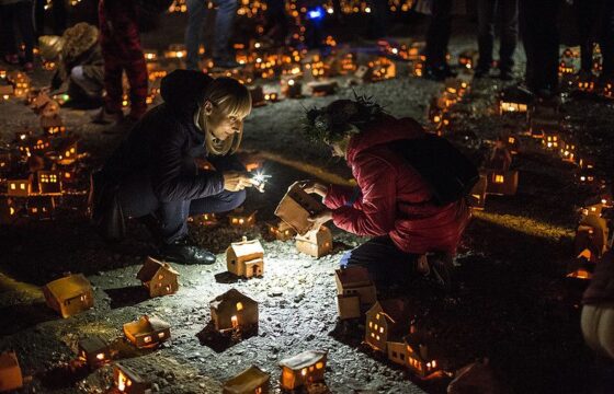 Miniaturowe gliniane domki. Jest ich bardzo dużo. Rozstawione są na ziemi na dużej przestrzeni, wewnątrz nich palą się malutkie świeczki. Pośród nich wędrują ludzie