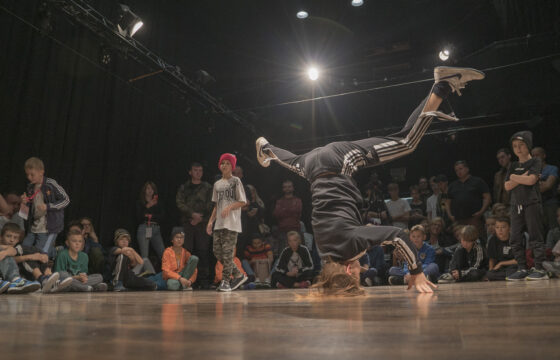 Chłopak tańczący breakdance - za nim na podłodze siedzi publiczność