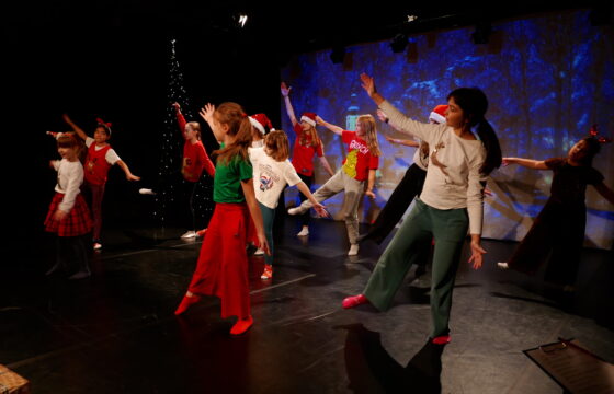 Grupa kilkuletnich dzieci tańczy na scenie w bożonarodzeniowej scenografii