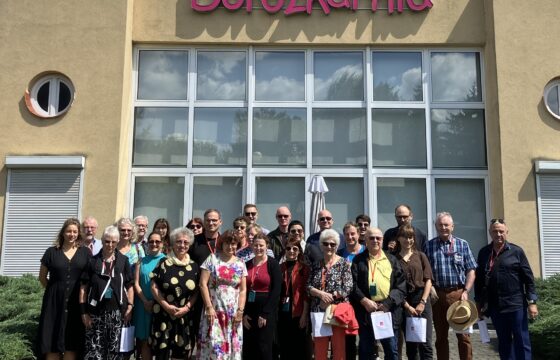 Grupa osób w róznym wieku pozuje do zdjęcia przed budynkiem z neonem Dorozkarnia. Wszyscy są w letnich ubraniach.