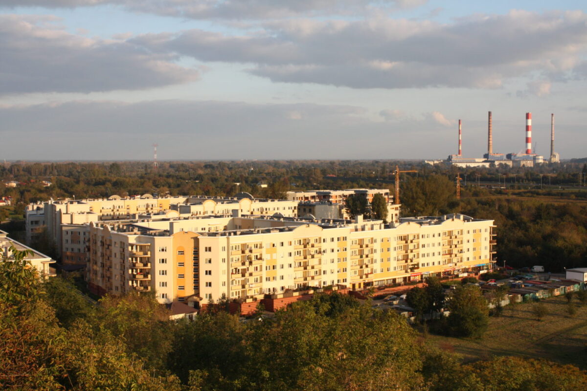 Zdjęcie z lotu ptaka osiedle bloków wśród drzew, w tle kominy elektrowni